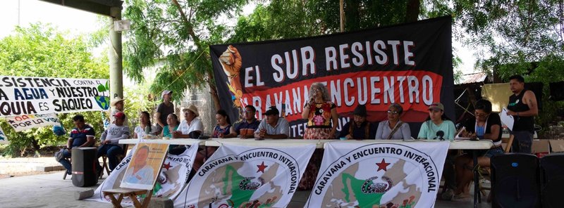 Podium und Redner:innen vor einem Plakat von El Sur Resiste
