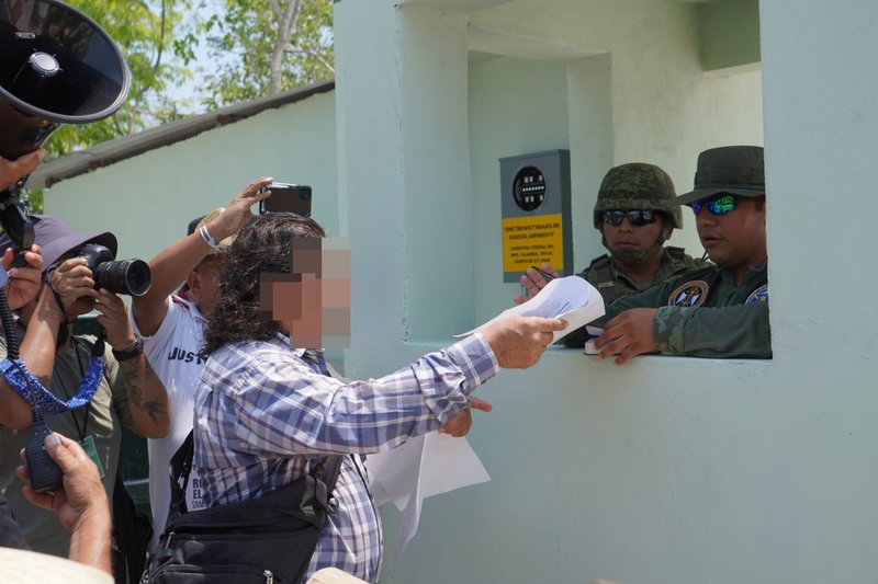 Ein Mann übergibt Soldaten ein Dokument. Er wird von der Presse begleitet